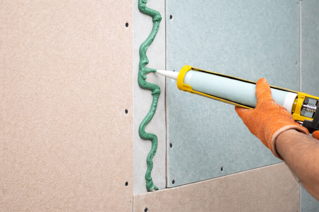 Green damping compound applied between two layers of drywall to help block wall noise